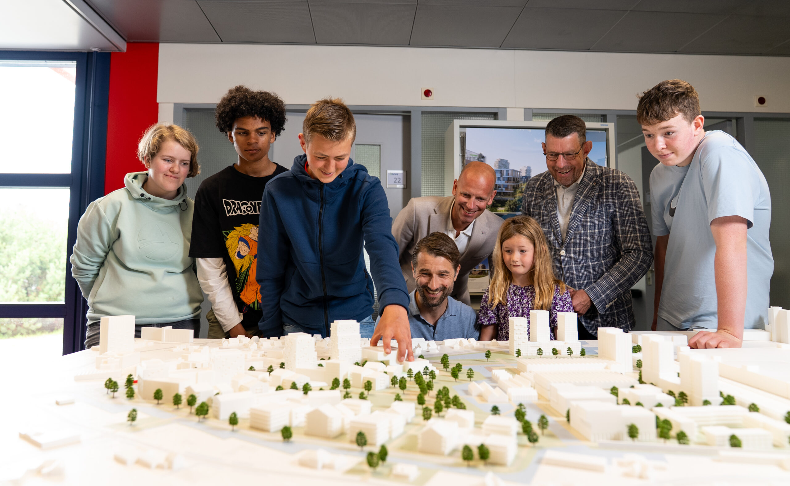 ISW - Een groep volwassenen en leerlingen verzamelt zich rond een grote bouwmaquette van een stad op Flora Campus Westland en observeert en bespreekt de miniatuurgebouwen en bomen. Een jongen wijst naar de maquette terwijl anderen geïnteresseerd toekijken.